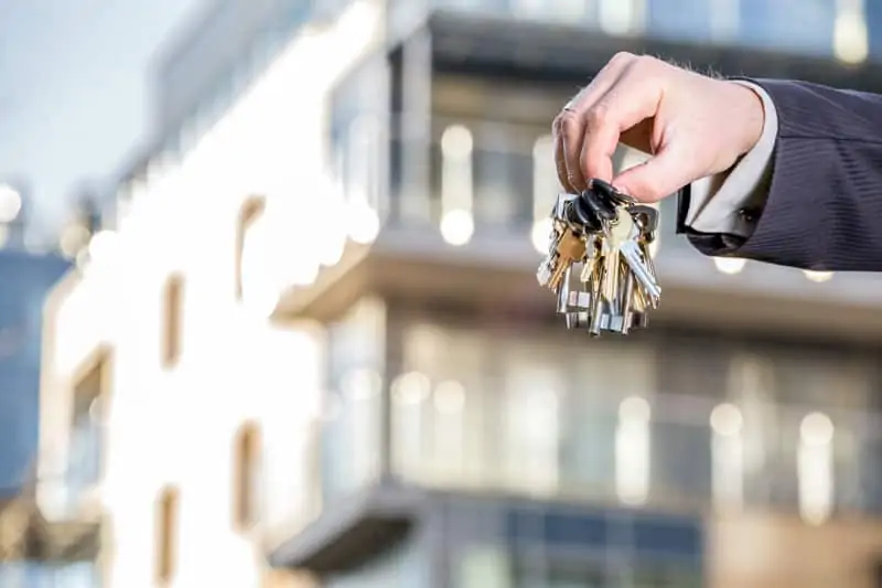 Property agent holding keys in front of residential properties